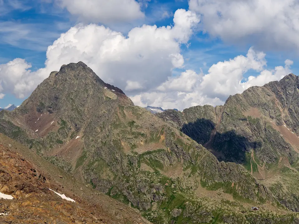 Grasige Hänge und felsige Gipfel in den Stubaier Alpen unter Wolken