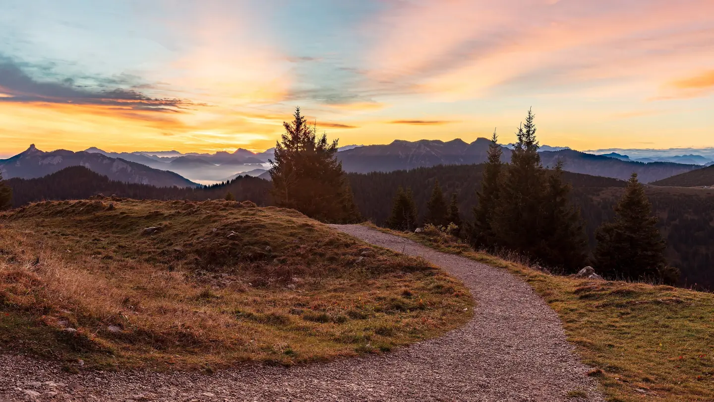 Sonnenaufgang über einem Wiesenweg in den Chiemgauer Alpen, Nebel liegt in den Tälern