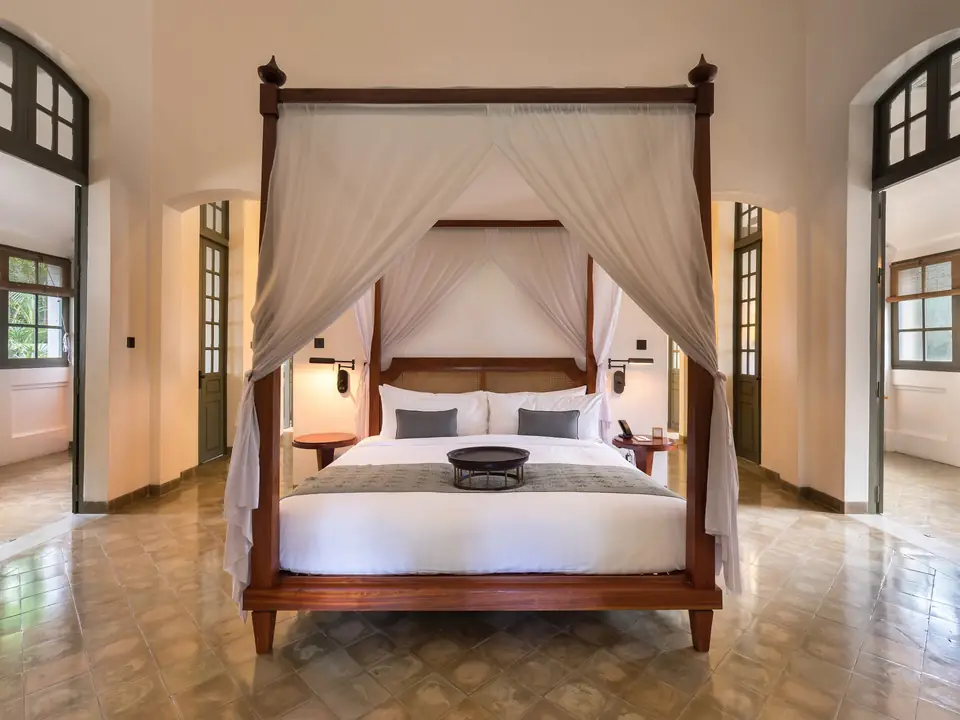 Himmelbett mit weißen Vorhängen in einer hellen Suite